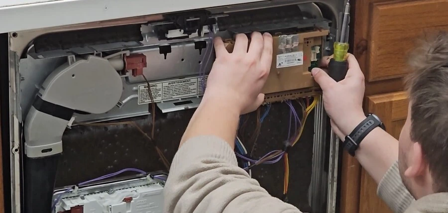 Technician repairing an appliance control panel with a screwdriver